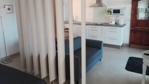 A modern kitchen with white cabinets, a microwave, and a coffee maker. There is a blue sofa and a wooden cabinet in the room. -  Studio for 2 people in Bages in the heart of the Narbonnaise Regional Natural Park (Bages)