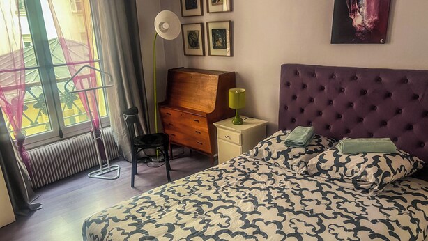 A bedroom with a bed, a dresser, a chair, a lamp, and a radiator. - Superb apartment in the Marais (Paris)