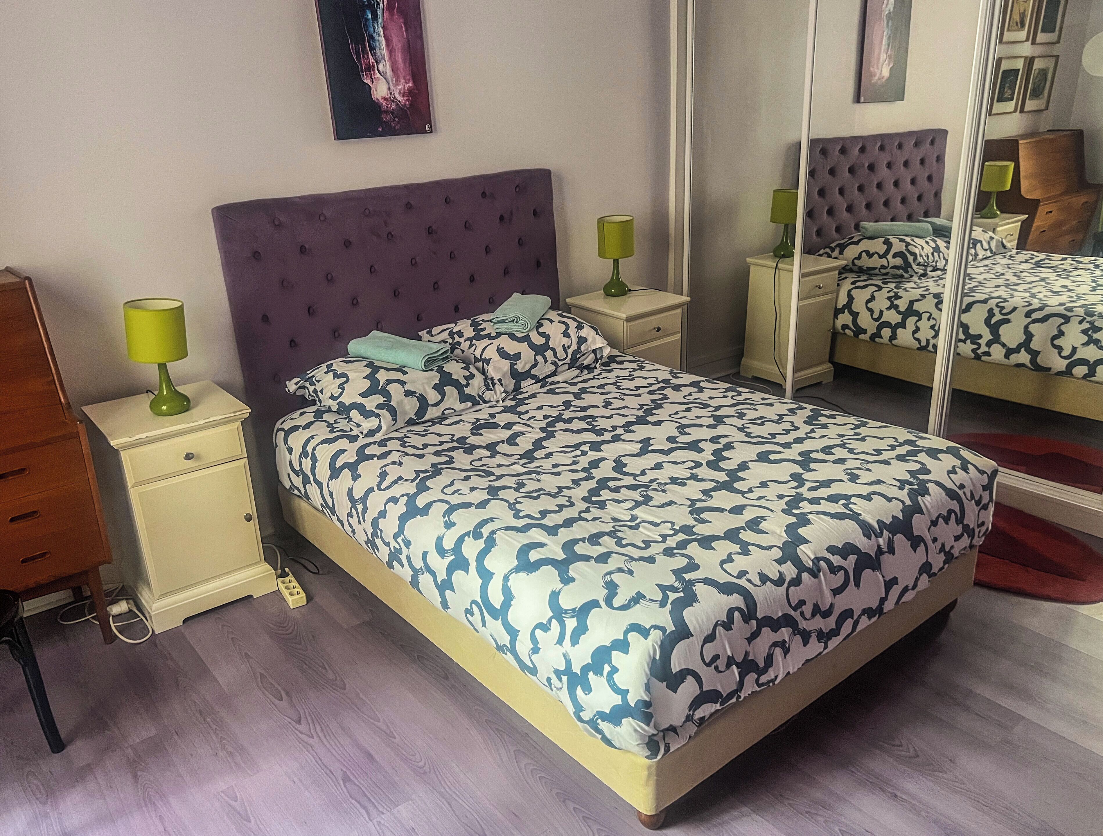 A bedroom with a large bed, a nightstand with a lamp, a dresser, and a mirror.