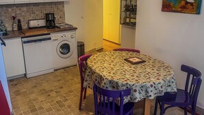 A compact kitchen with a washing machine, a coffee maker, and a dining table with purple chairs. - Superb apartment in the Marais (Paris)