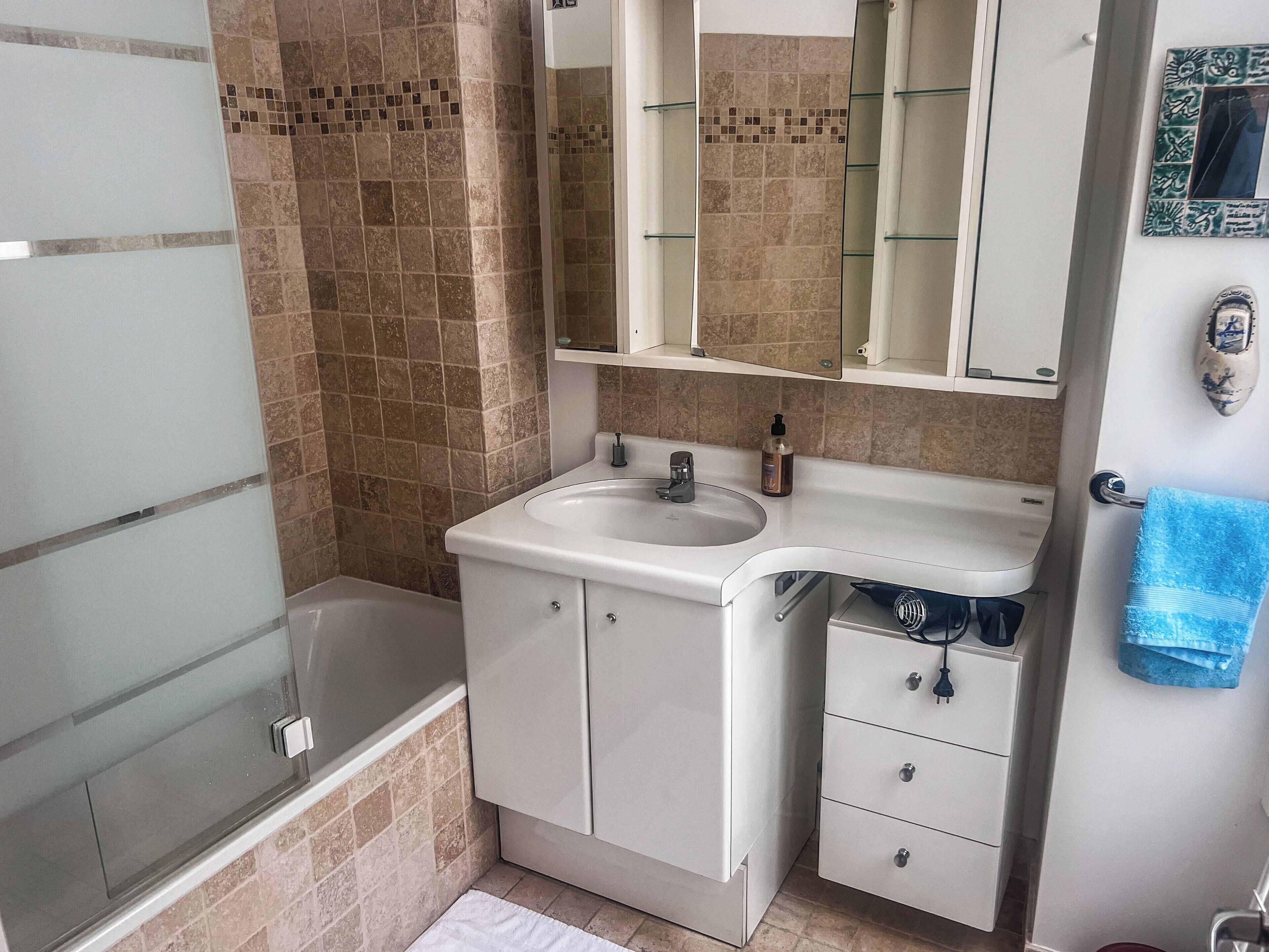 A bathroom with a bathtub, a sink, a mirror, and a towel rack.