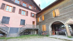 A building with a pink facade, wooden shutters, and a staircase leading to a balcony.
