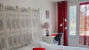 A neatly made bed with two red pillows, a desk with a lamp, and a chair. - Meublé de tourisme ** "chezphoenixette (Nieuil)