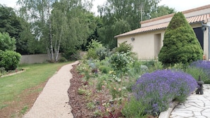 A garden pathway leading to a house with a tiled roof, surrounded by various plants and a neatly trimmed hedge. - Meublé de tourisme ** "chezphoenixette (Nieuil)