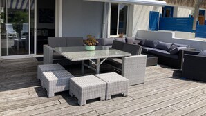 Une terrasse extérieure avec une porte vitrée donnant sur un espace de détente abrité, aménagé avec une table, des chaises et des canapés.
