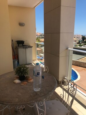 A balcony with a round table, a potted plant, a water bottle, and a chair.