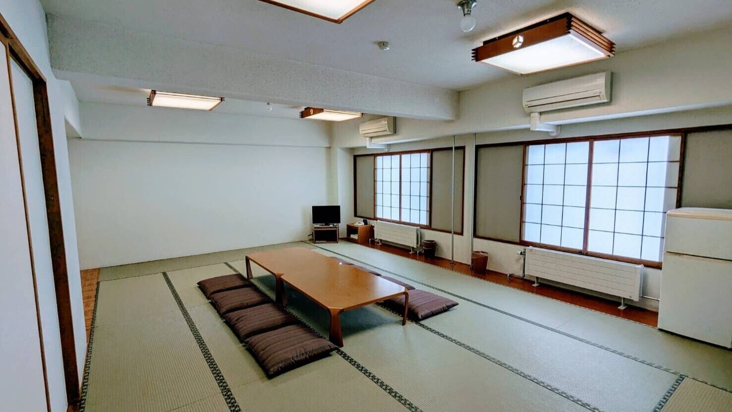 Ein Konferenzraum mit einem langen Tisch, Tatami-Matten, einem Fernseher und großen Fenstern.