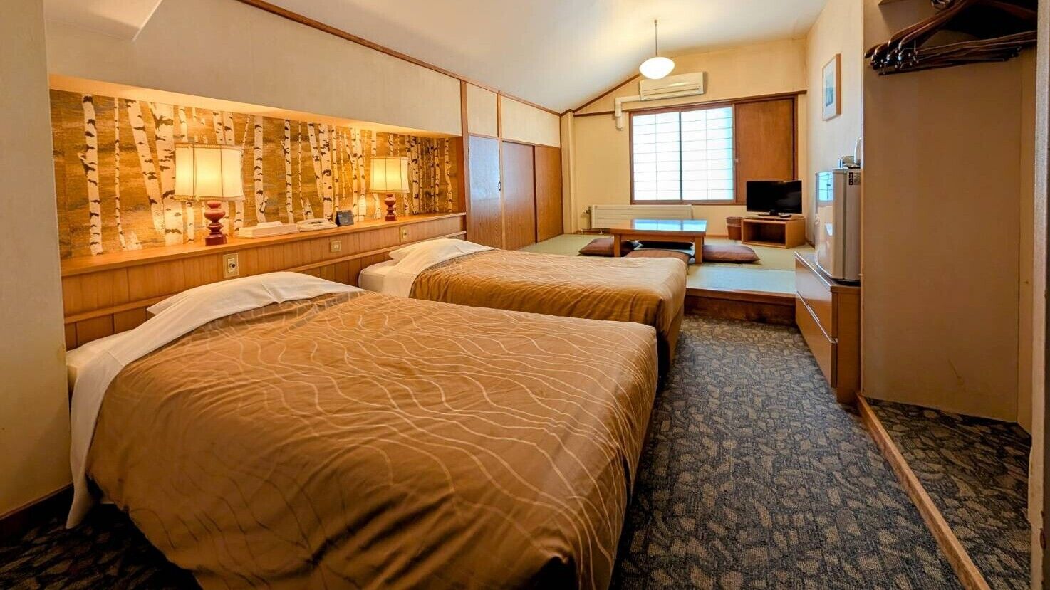 Ein Hotelzimmer mit zwei Betten, einem Fernseher, einem Schreibtisch und einem großen Fenster.