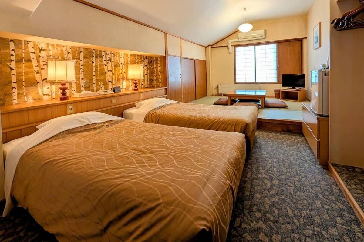 Ein Hotelzimmer mit zwei Betten, einem Fernseher, einem Schreibtisch und einem großen Fenster.