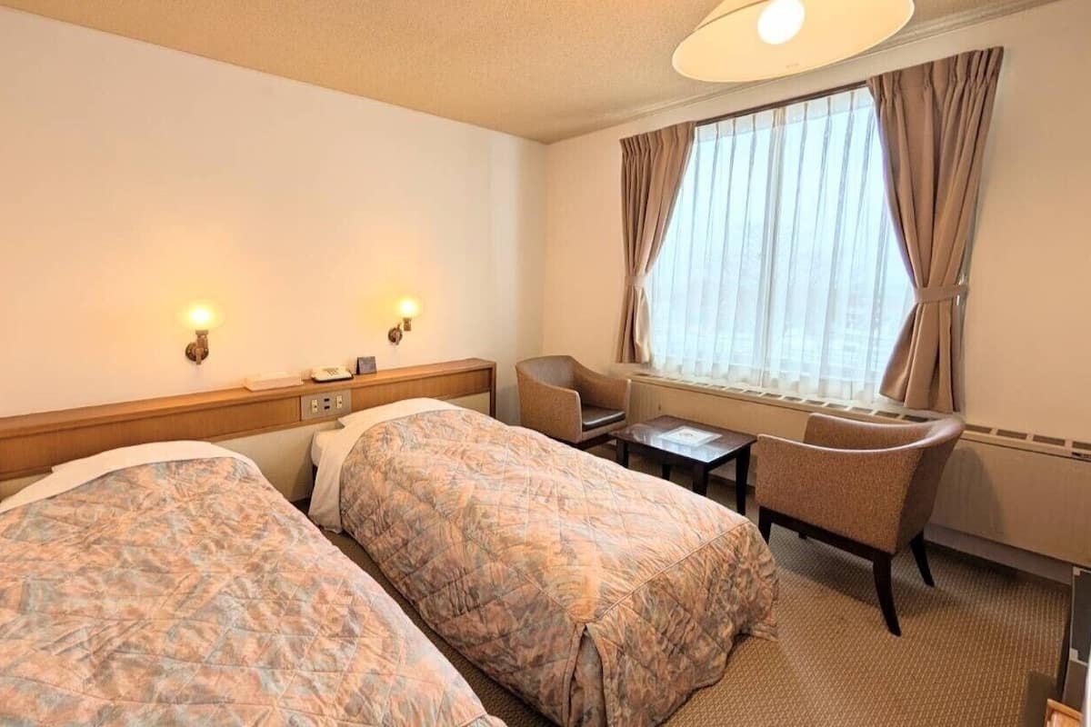 Ein Hotelzimmer mit zwei Betten, einem Schreibtisch, einem Stuhl und einem Fenster mit Vorhängen.