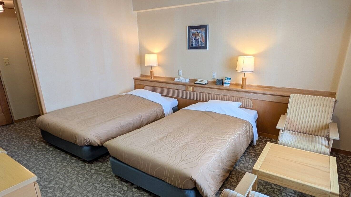 Ein Hotelzimmer mit zwei Betten, einem Sessel, einem kleinen Tisch und einer Wandlampe.