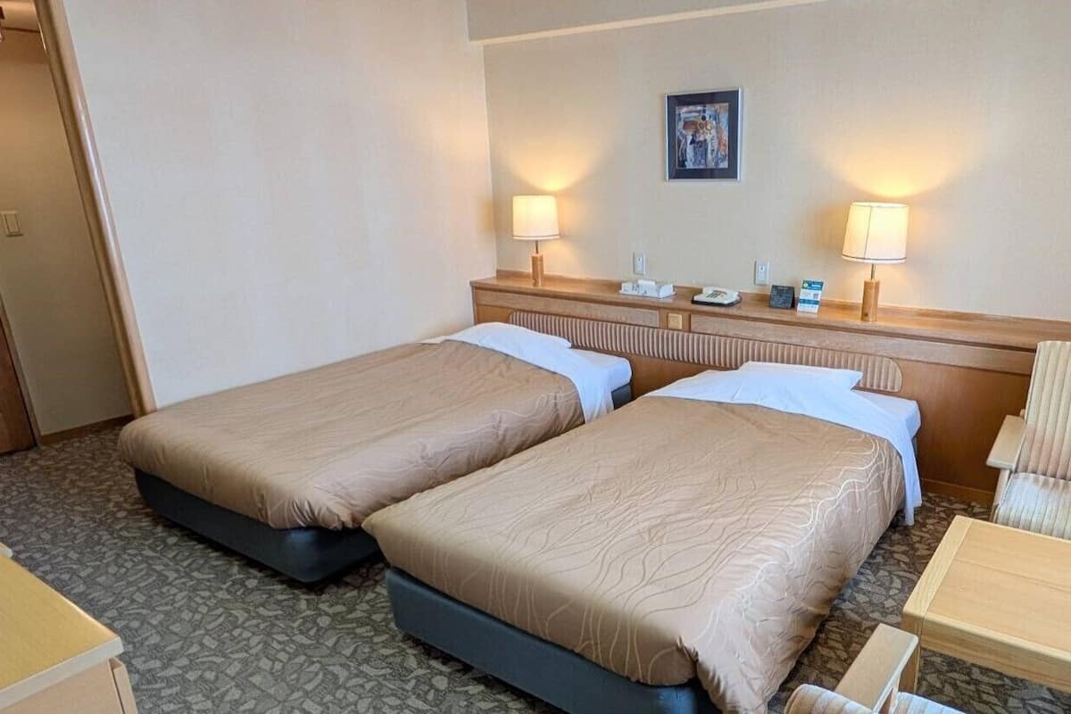 Ein Hotelzimmer mit zwei Betten, einem Sessel, einem kleinen Tisch und einer Wandlampe.