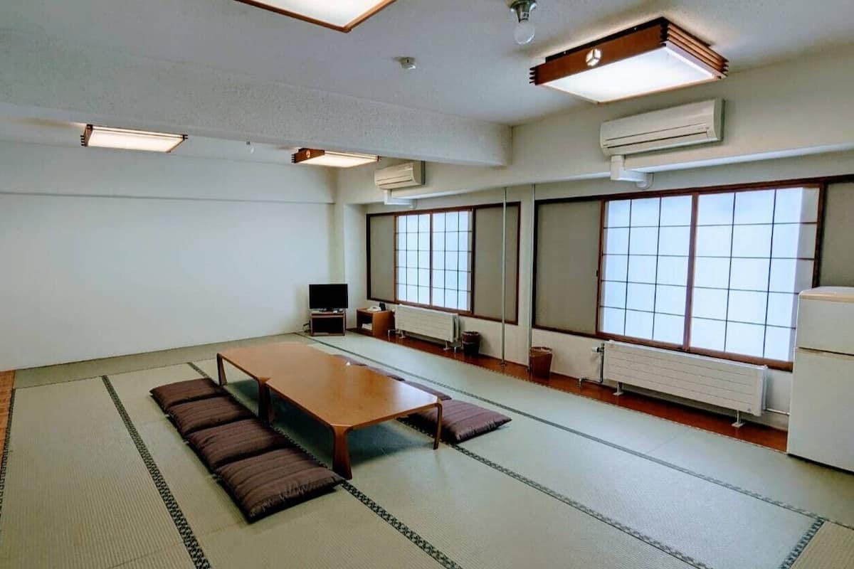 Ein Konferenzraum mit einem langen Tisch, Tatami-Matten, einem Fernseher und großen Fenstern.