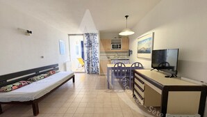 A compact room with a bed, a desk, a chair, a television, and a kitchenette.