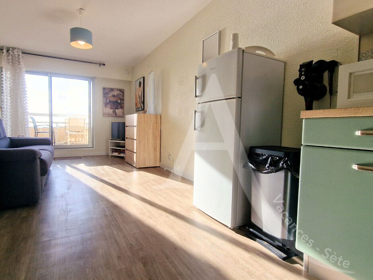Een moderne keuken met een koelkast, magnetron en een afvalbak. Er is een houten kastje en een lichtkleurig aanrecht.