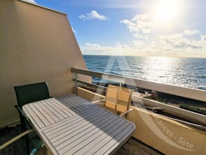 Een balkon met een tafel en stoelen, met uitzicht op de zee.