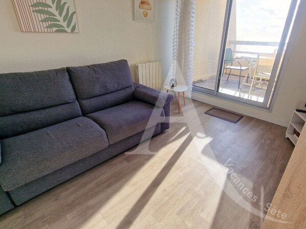 Een moderne woonkamer met een grijze bank, een kleine tafel en uitzicht op de zee door een groot raam.