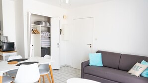 Un salon moderne avec un canapé gris, des chaises blanches, une petite table blanche et un coin cuisine équipé d’un four à micro-ondes et d’une machine à café.