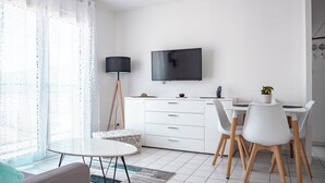 Un salon moderne et minimaliste, avec un canapé blanc, une table basse ronde et un coin repas comprenant une table et des chaises blanches.