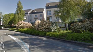 Une rue résidentielle bordée d’immeubles d’appartements, avec un ciel dégagé et des haies bien entretenues.