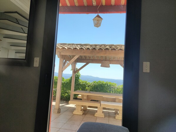 A wooden pergola with a tiled roof and a bench, overlooking a mountainous landscape.