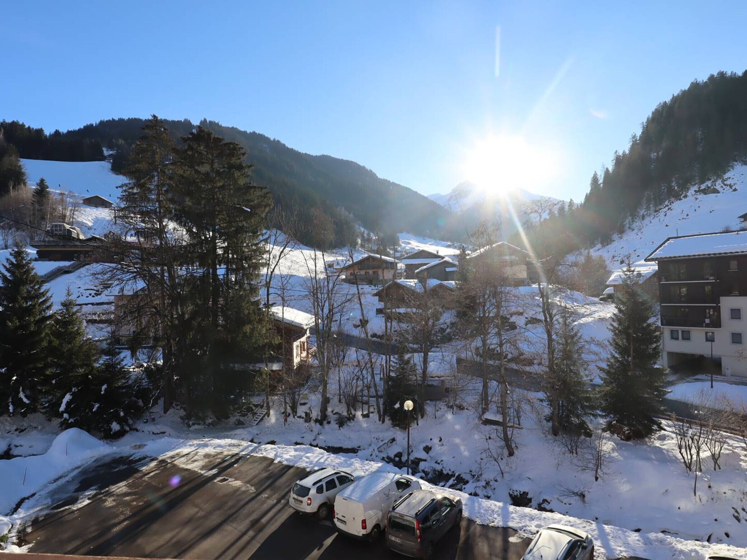 Un village de montagne enneigé, avec des bâtiments, un espace de stationnement et un ciel dégagé.