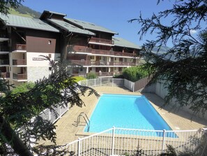 A hotel with a swimming pool, multiple balconies, and a view of the surrounding landscape.