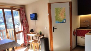 A compact room with a TV, a map, a small kitchen, and a dining area with a table and chairs.