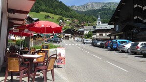 A street with outdoor seating, parked cars, and buildings with traditional architecture.