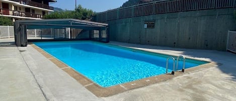 A rectangular swimming pool with a concrete deck, a metal ladder, and a view of a mountain in the background.