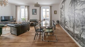 Un salon moderne avec une table à manger en verre, un canapé en cuir et une grande fresque représentant un paysage tropical.