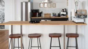 Une cuisine moderne avec un comptoir-bar en bois, trois tabourets, un réfrigérateur en acier inoxydable et une machine à café.