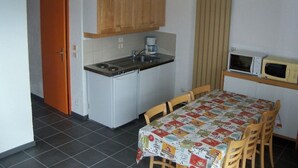 Eine kleine Küche mit Herd, Mikrowelle und Holzschränken. Ein Esstisch mit Stühlen und einer gemusterten Tischdecke steht bereit.