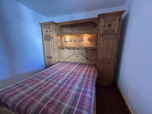 A bedroom with a wooden headboard, a plaid bedspread, and two wall-mounted lamps.