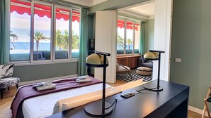 A bedroom with a bed, bedside lamps, a desk, and a view of the ocean through large windows. - N&J - LAGOON PROMENADE - Central - Sea front (Niza)