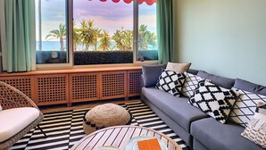 A room with a view of palm trees and the sea through large windows, a sofa with patterned cushions, a wicker chair, and a round wooden table. - N&J - LAGOON PROMENADE - Central - Sea front (Niza)