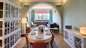 A dining area with a white table set for four, surrounded by red and white patterned chairs. There is a white cabinet with glass doors on the left, and a white console table with drawers on the right. - N&J - LAGOON PROMENADE - Central - Sea front (Niza)