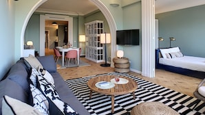 A modern hotel room with a large sofa, a dining area with a table and chairs, a TV mounted on the wall, and a bed with a headboard. - N&J - LAGOON PROMENADE - Central - Sea front (Niza)