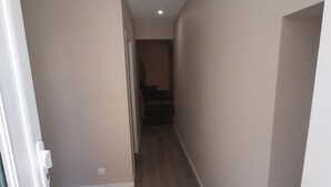 Un pasillo con suelo de madera, paredes color beige y una puerta blanca a la izquierda.