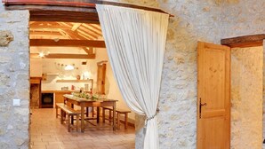 A rustic stone-walled room with a wooden door, a dining area with a table and benches, and a curtain hanging over the doorway. - Charming cottage for 12 people - Wilderness + private pool (Thézac)