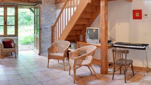 A cozy room with a stone wall, wooden staircase, wicker chairs, a television, and a keyboard. - Charming cottage for 12 people - Wilderness + private pool (Thézac)