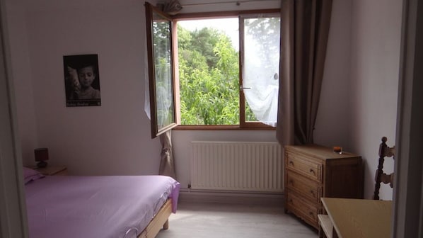 Une chambre avec un lit simple, une commode, un radiateur et une fenêtre avec des rideaux.