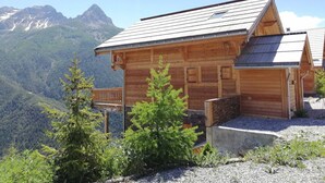 A wooden cabin with a sloped roof, a balcony, and a view of a mountainous landscape.