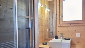 A wooden cabin bathroom with a glass shower door, a white sink, and a mirror above it.