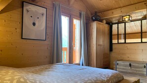 A cozy bedroom with a large bed, wooden walls, a bear painting, and a wardrobe.