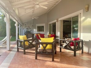 A covered patio area with wicker furniture, a ceiling fan, and a view of the outdoors.