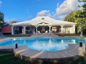 A house with a swimming pool, lounge chairs, and a covered patio area.