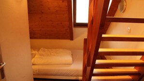 Una habitación pequeña y acogedora con una cama individual, una escalera de madera y un ventanal que deja entrar luz natural.