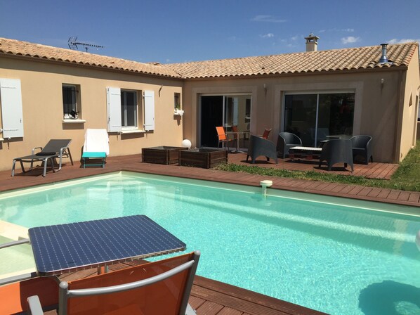 A swimming pool with a table and chairs, a covered patio area with seating, and a building with windows and a chimney. - House beautiful living room, 3 bedrooms with heated pool in La Rochelle (La Rochelle villedoux)