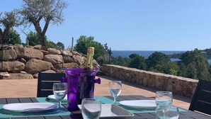 A table set outdoors with a view of the sea, a purple cooler, and a bottle of champagne.